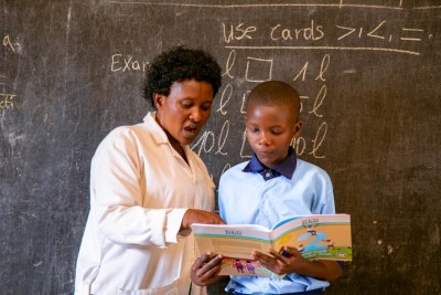 A teacher helps a child while reading a book at Ecole Primaire Kimisange (file photo).